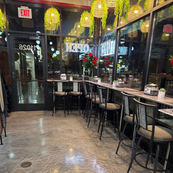 Interior of Baba Saj, showing a row of bar stools along a window counter with hanging green lights.