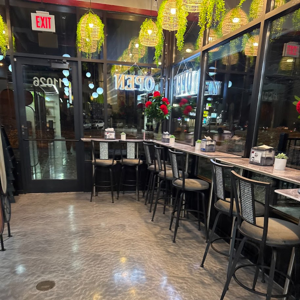 Interior of Baba Saj, showing a row of bar stools along a window counter with hanging green lights.