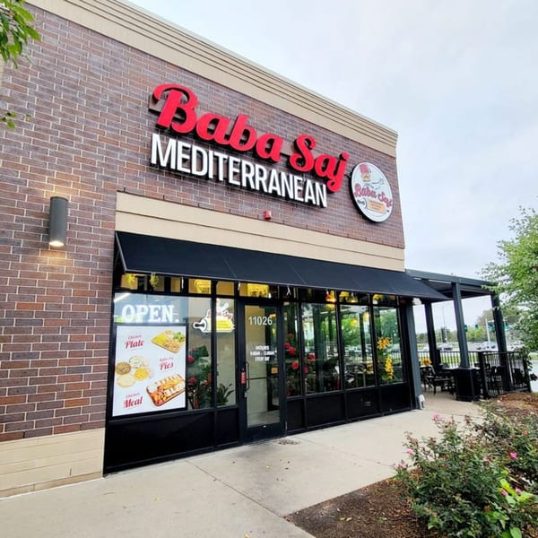 The exterior of Baba Saj Mediterranean restaurant, featuring a brick facade, large windows, and an outdoor patio.