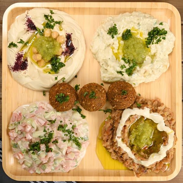 A wooden tray with four Mediterranean dishes: hummus, baba ghanoush, falafel, and a vegetable salad.
