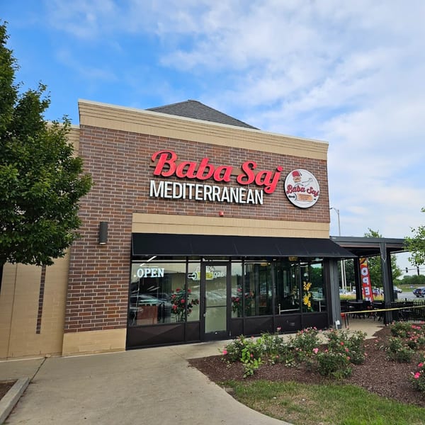 Exterior of Baba Saj Mediterranean restaurant with a brick facade, black awning, and outdoor seating.