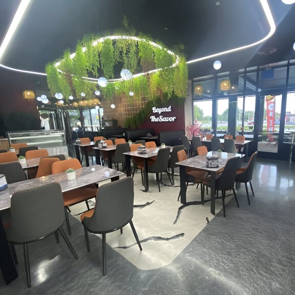 Modern Baba Saj dining room with orange and gray chairs, marble tables, and hanging greenery.