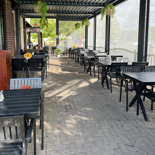 Outdoor patio at Baba Saj with black tables and chairs, hanging plants, and a brick wall.
