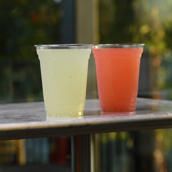 Two plastic cups, one with yellow and one with red drink, sit on a table.