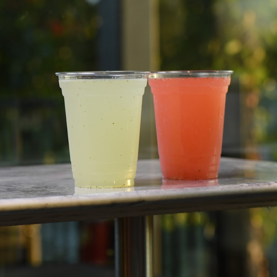 Two plastic cups, one with yellow and one with red drink, sit on a table.