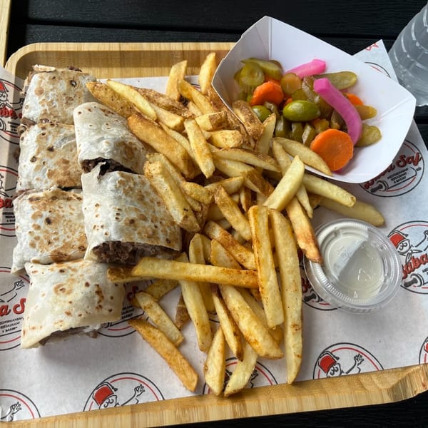 Baba Saj Mediterranean shawarma wraps, fries, and pickled vegetables on a wooden tray.