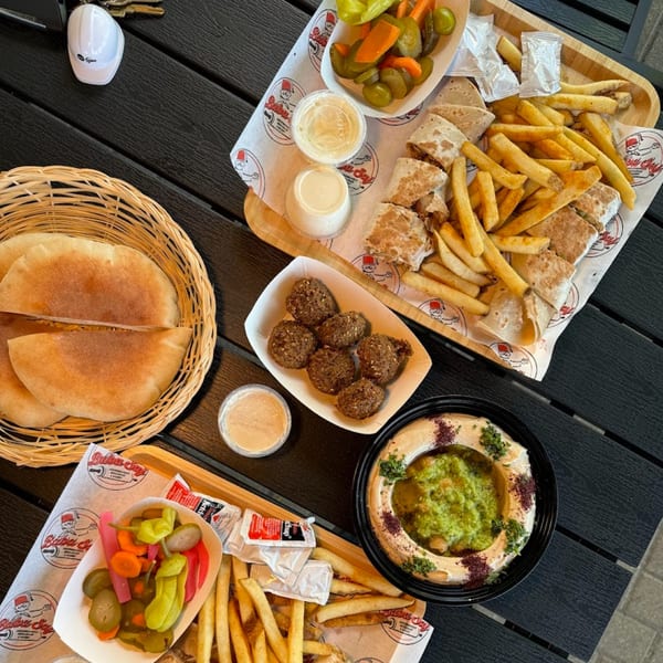A table laden with Baba Saj's Mediterranean feast: shawarma, fries, falafel, hummus, pita, and pickles.