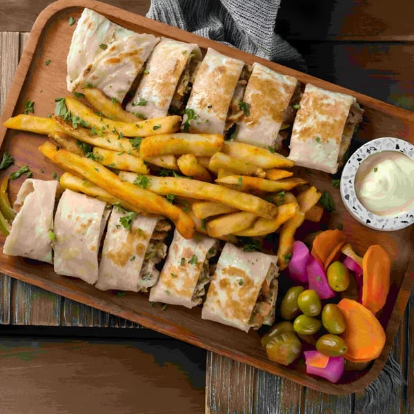Baba Saj's chicken shawarma wraps, fries, pickled vegetables, and garlic sauce on a wooden tray.