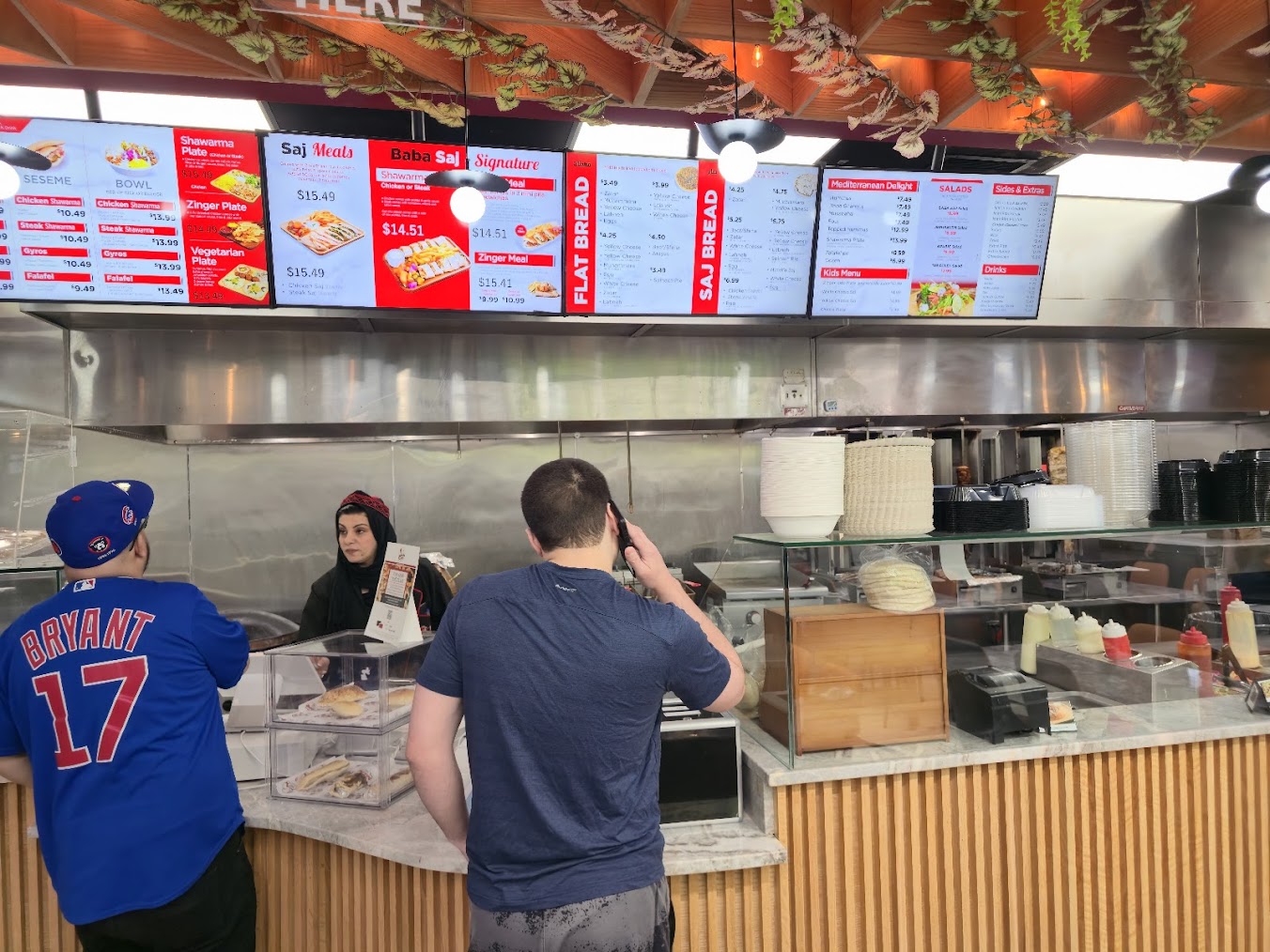 Interior view of Baba Saj Mediterranean Restaurant’s ordering counter with digital menu screens showcasing various dishes.